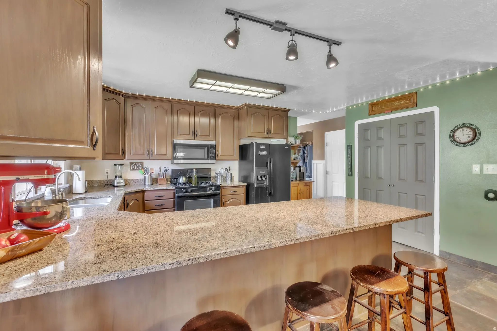 Kitchen featuring black appliances, a breakfast bar area, a peninsula, light stone countertops, and wood finish cabinetry