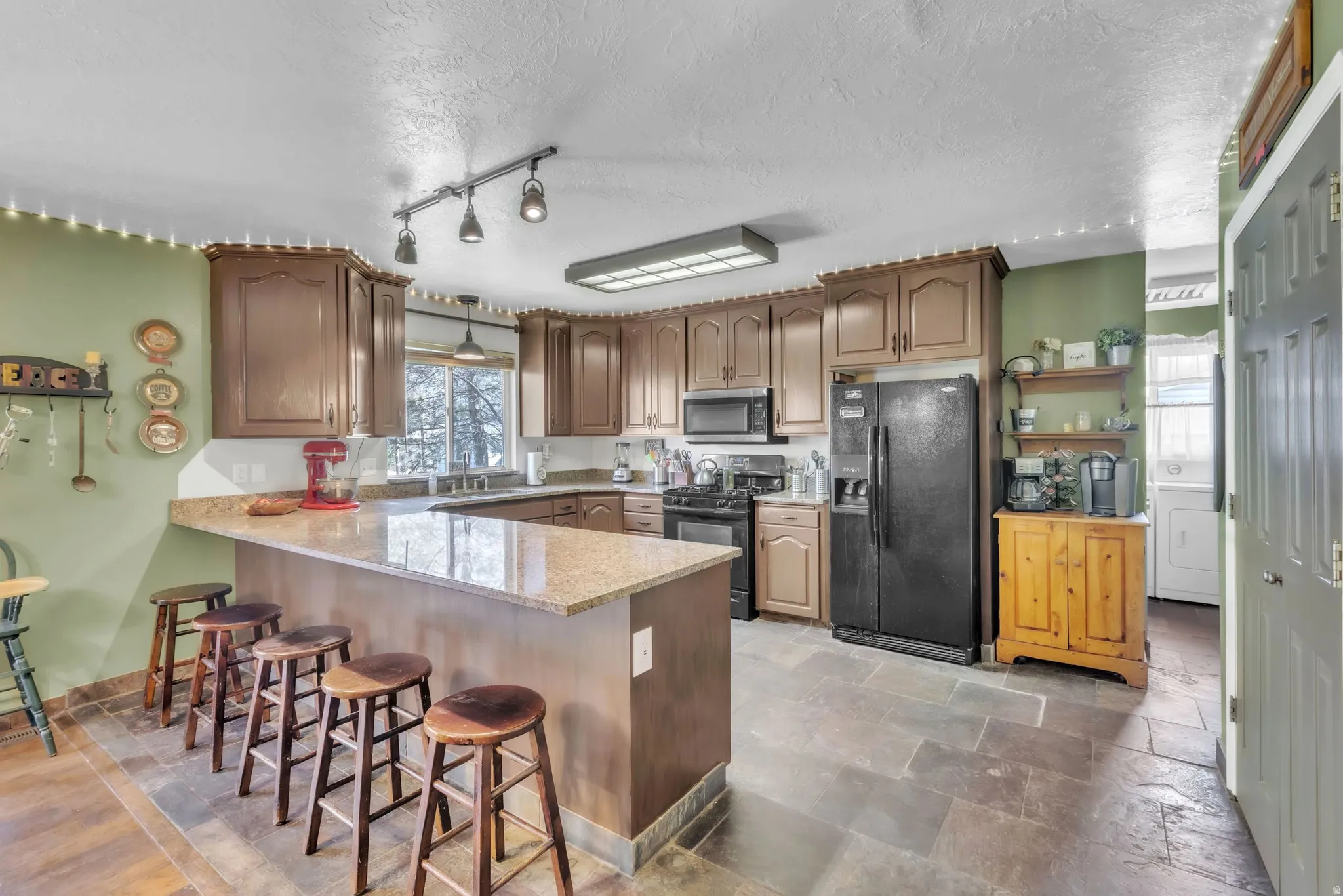 Kitchen with black appliances, a peninsula, a kitchen breakfast bar, rail lighting, and a textured ceiling