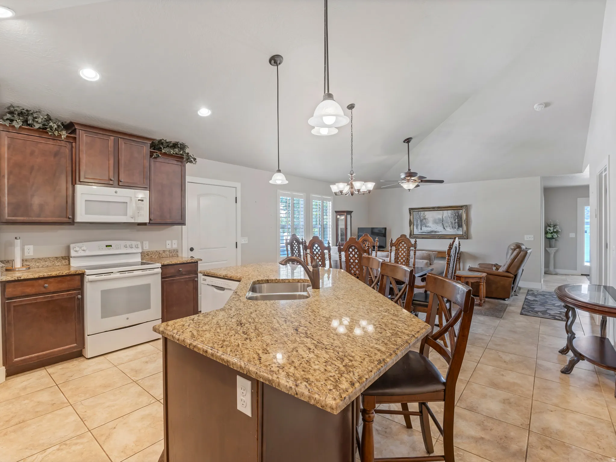 Kitchen featuring white appliances, light stone countertops, a ceiling fan, a center island with sink, and vaulted ceiling