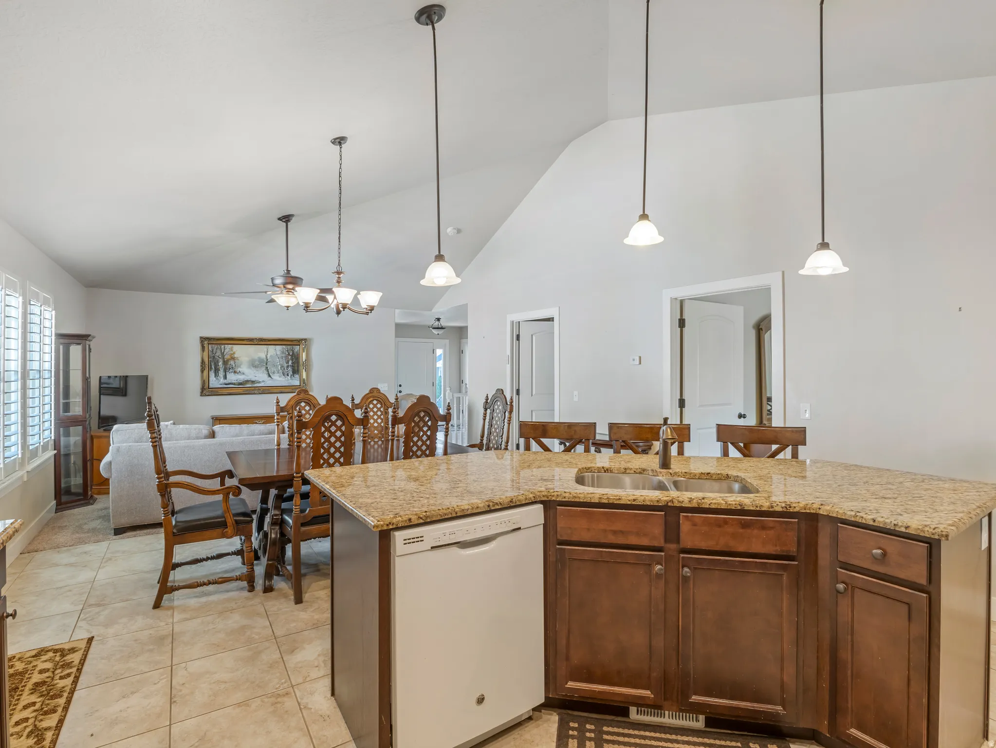 Kitchen featuring white dishwasher, a center island with sink, light stone countertops, hanging light fixtures, and lofted ceiling
