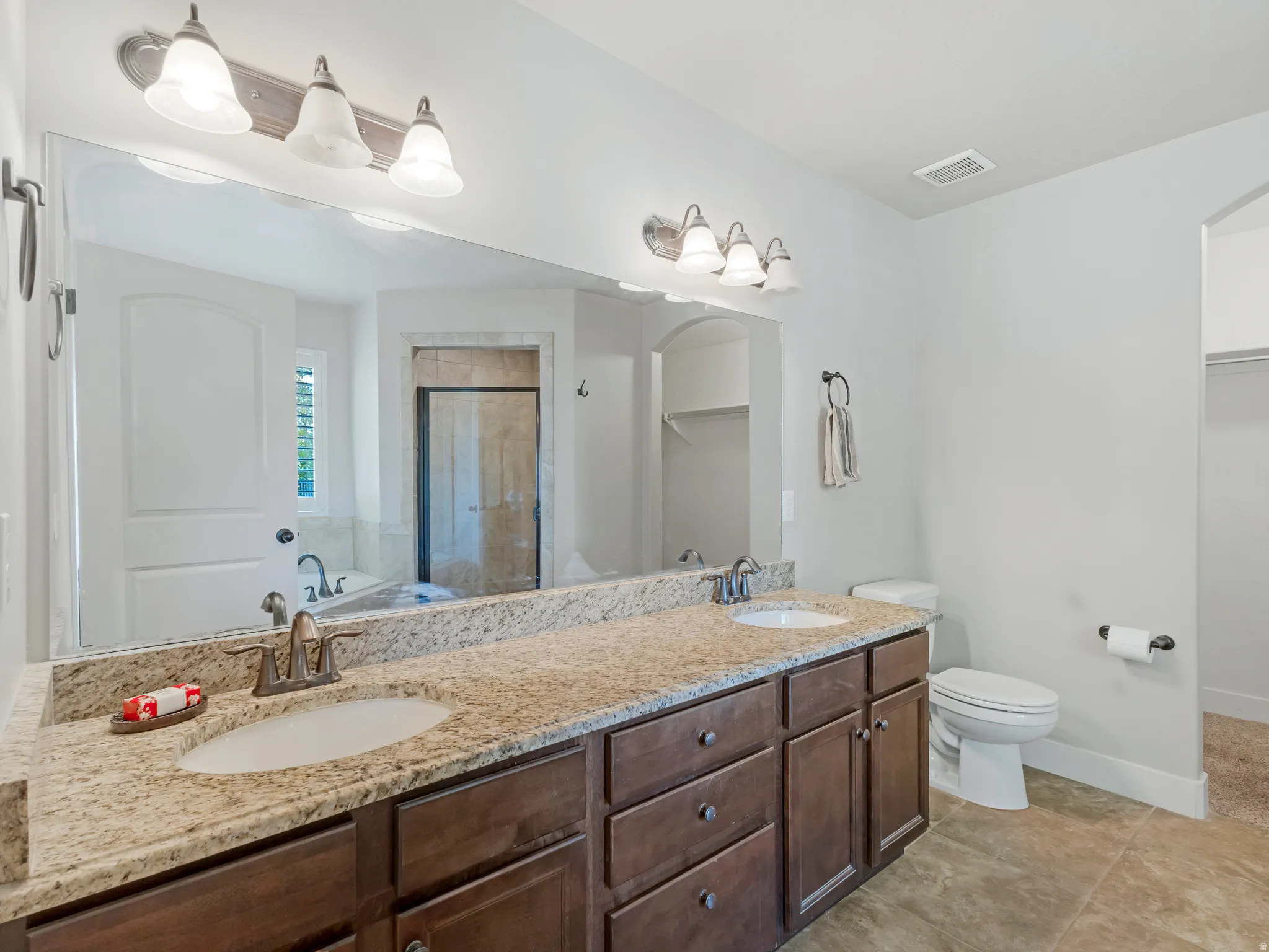 Full bathroom with double vanity, a shower stall, a garden tub, a spacious closet, and light tile patterned floors