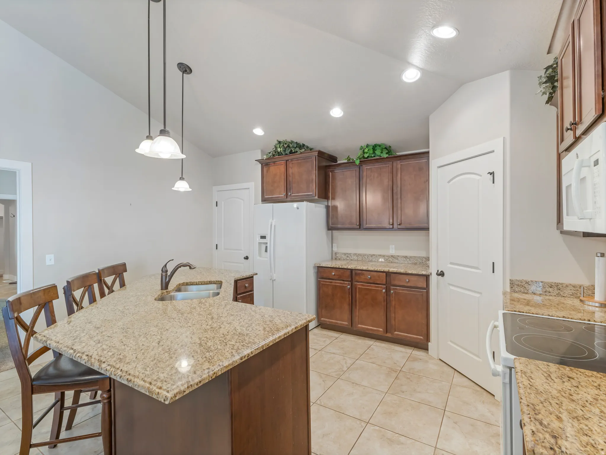 Kitchen featuring vaulted ceiling, a kitchen bar, white appliances, light stone countertops, and a kitchen island with sink