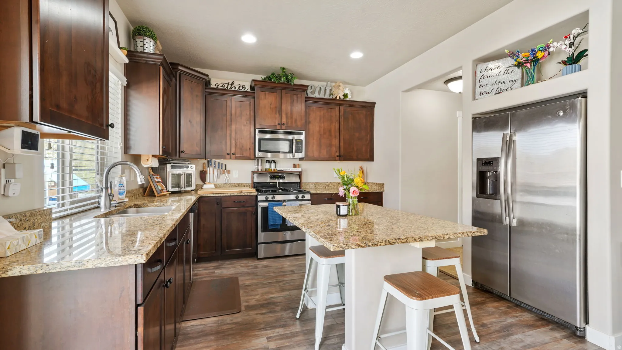 Kitchen with dark wood finish cabinets, stainless steel appliances, a breakfast bar area, light stone countertops, and recessed lighting