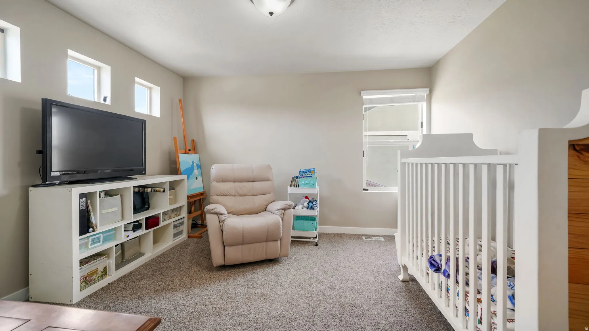 Bedroom with light colored carpet, a nursery area, and multiple windows