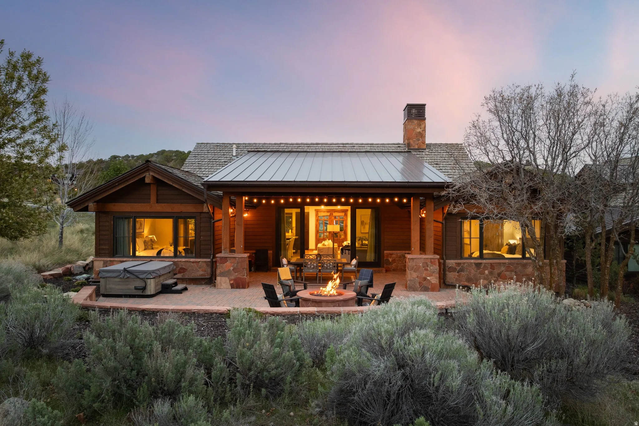 Back of house featuring a fire pit, a standing seam roof, a patio, a chimney, and a hot tub