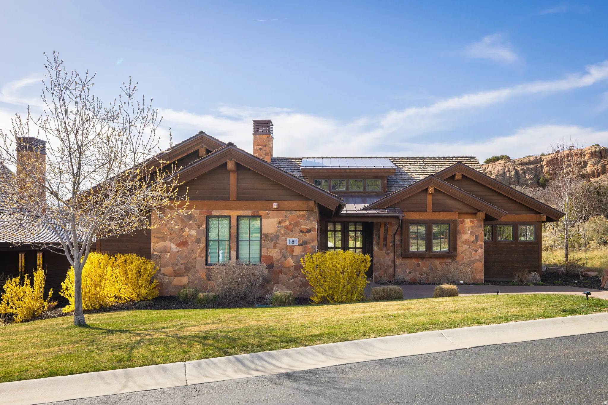 View of front of home featuring stone siding, a chimney, a front yard, and a standing seam roof