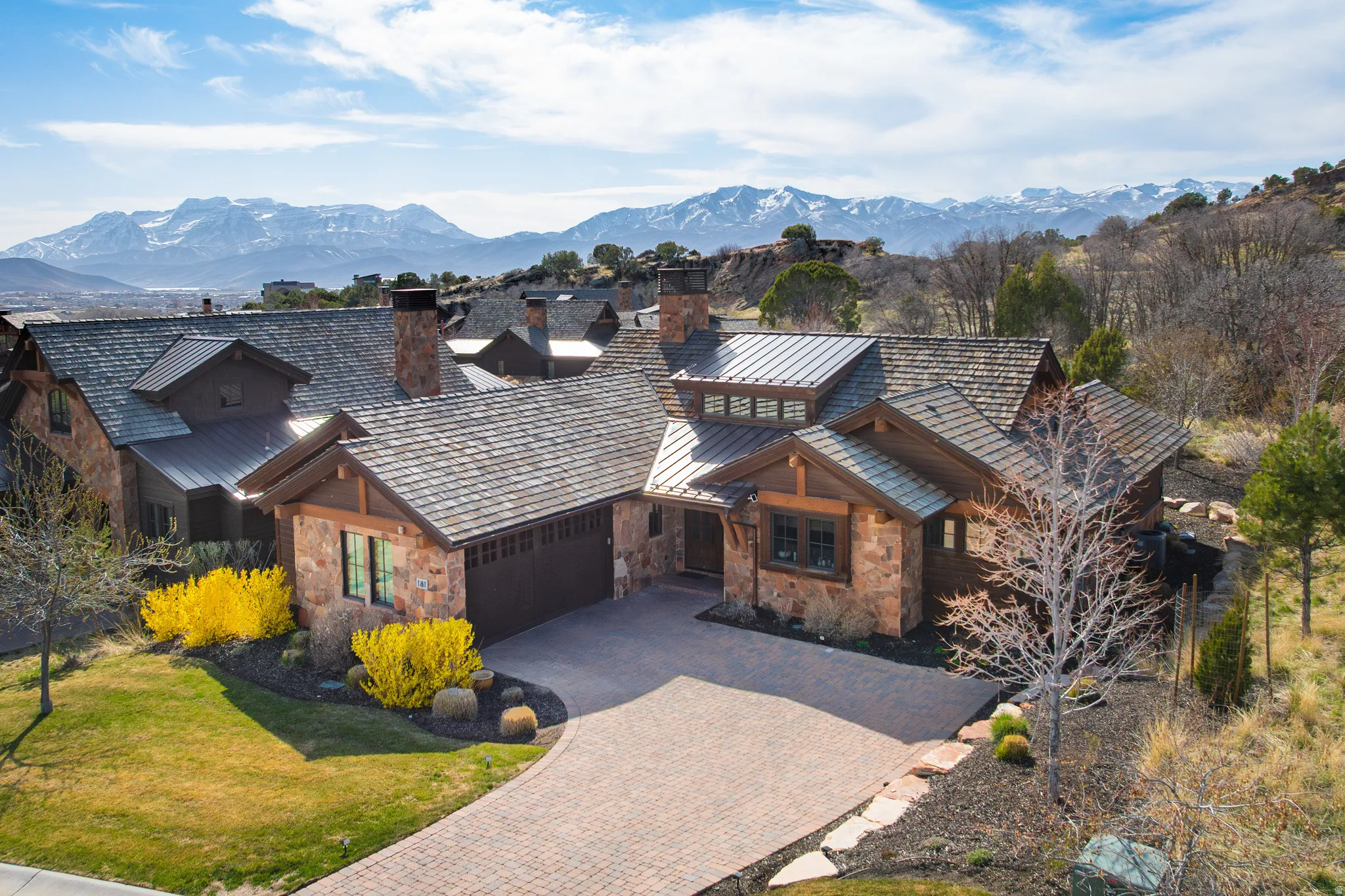 Rustic home featuring decorative driveway, stone siding, a garage, a standing seam roof, and a mountain view