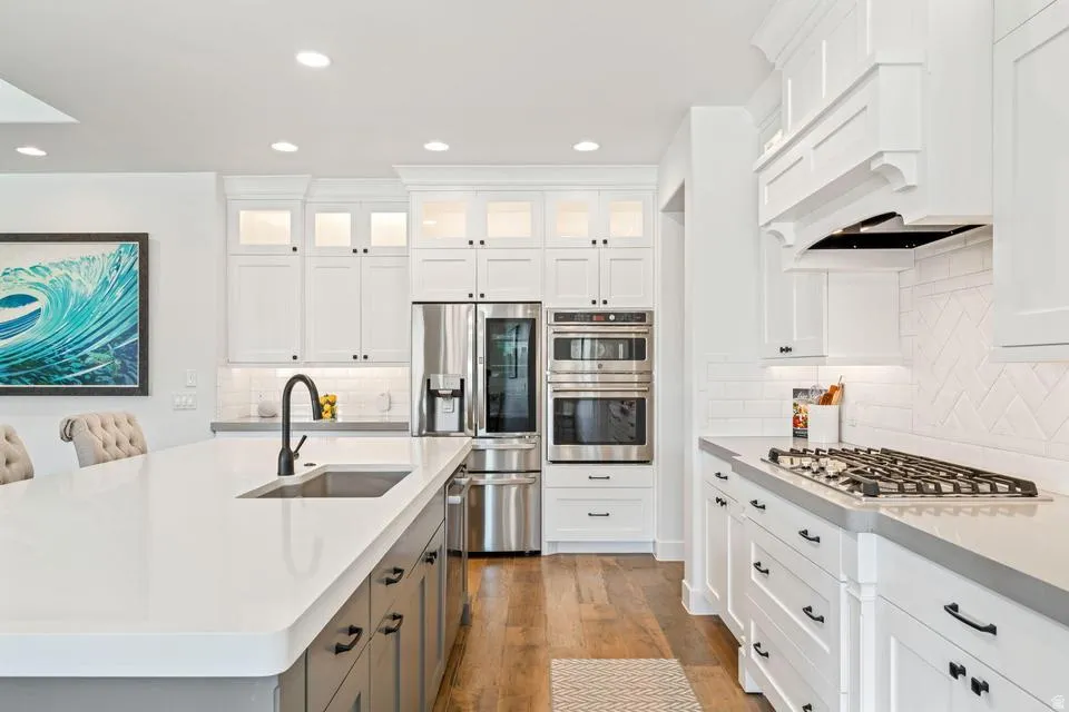 Kitchen featuring stainless steel appliances, light wood-type flooring, two tone cabinetry, recessed lighting, and light stone counters