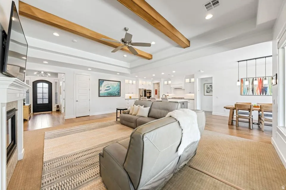 Living area featuring ceiling fan, beam ceiling, a fireplace, recessed lighting, and light wood-style flooring
