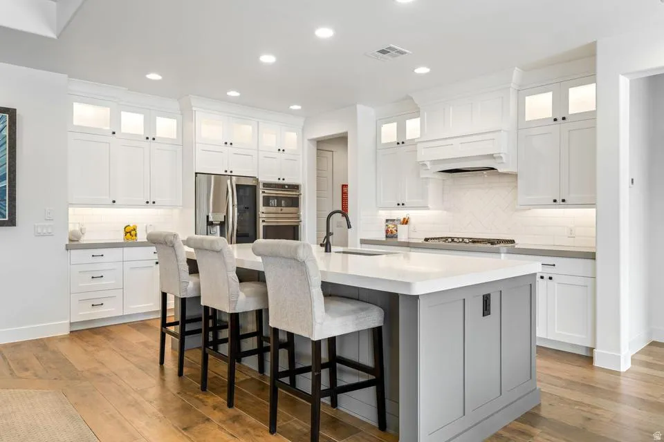 Kitchen with glass fronted cabinets, stainless steel appliances, a kitchen breakfast bar, recessed lighting, and an island with sink