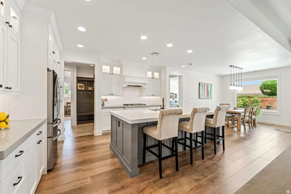 Two tone kitchen featuring a breakfast bar area, an island with sink, light wood-style floors, freestanding refrigerator, and two tone cabinetry