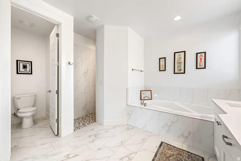 Bathroom featuring a bath, a marble finish shower, vanity, and light marble finish flooring