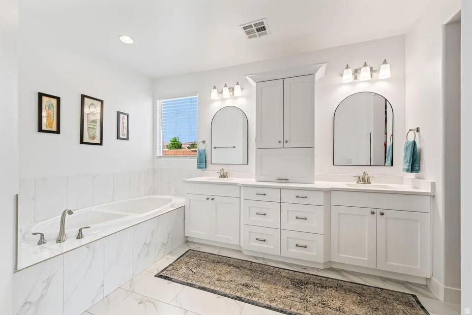 Full bath with double vanity, a bath, and light marble finish flooring