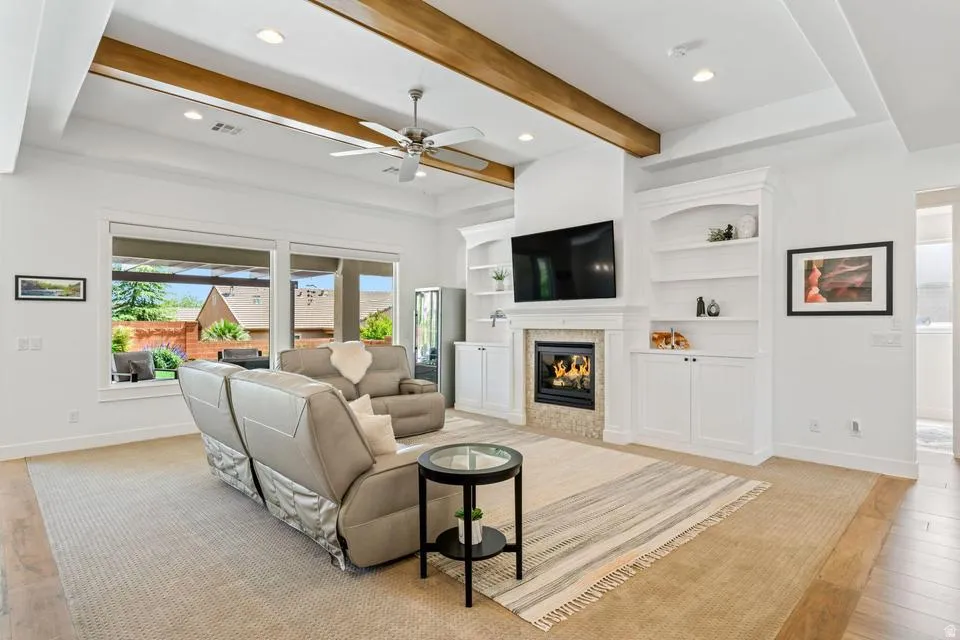 Living area with light wood-style flooring, a ceiling fan, beamed ceiling, a tile fireplace, and recessed lighting