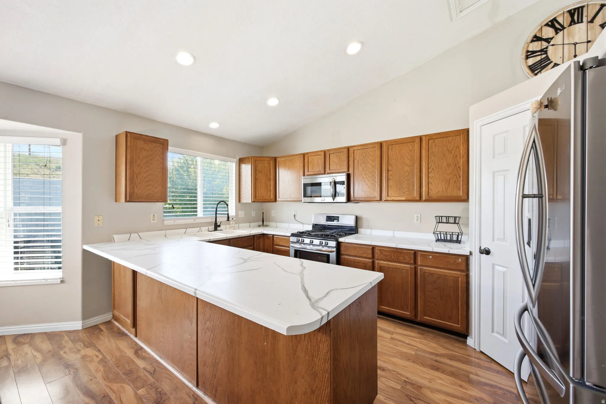 Kitchen with wood finish cabinets, stainless steel appliances, a peninsula, light countertops, and vaulted ceiling