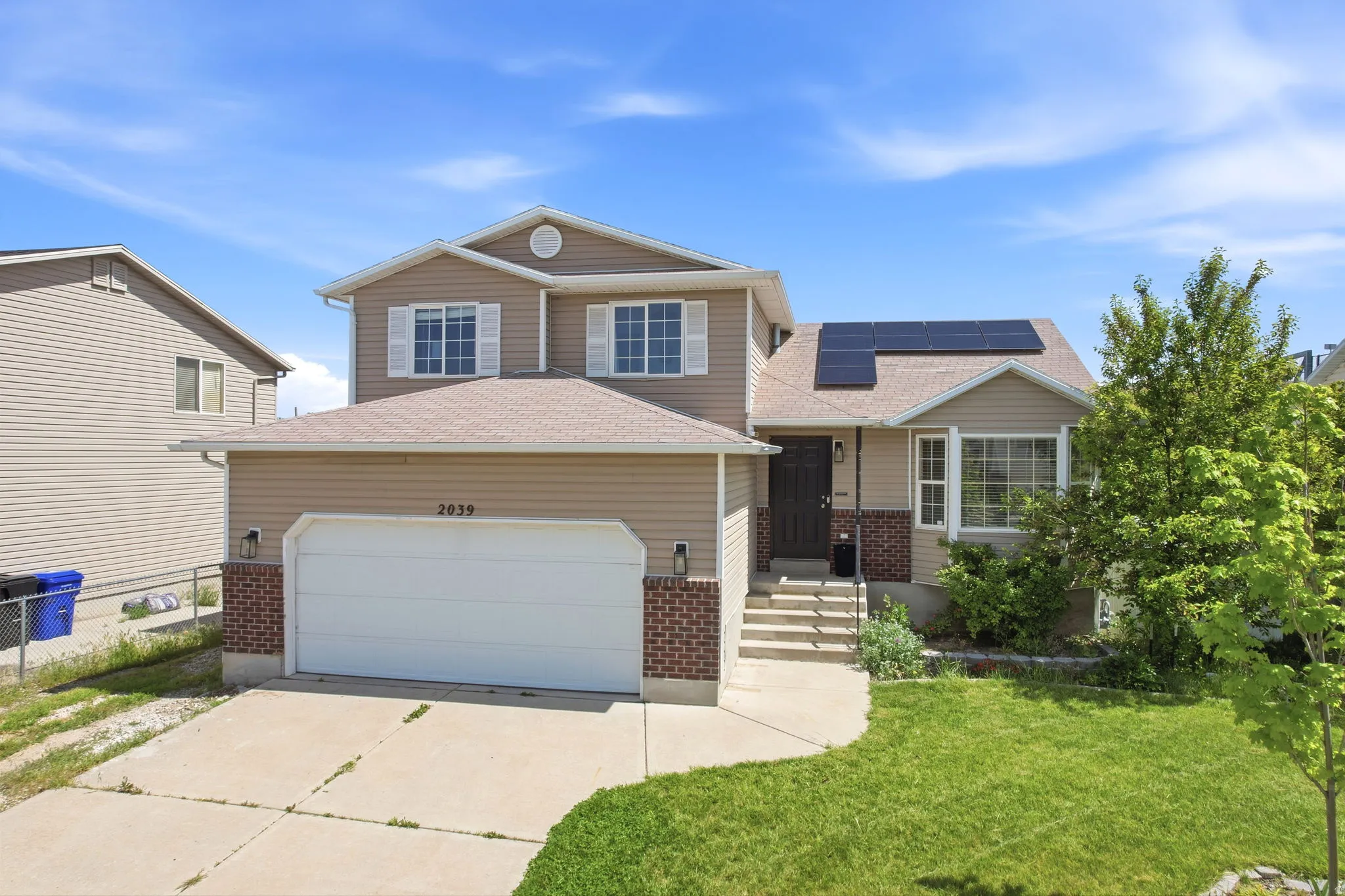 View of front of home with brick siding, concrete driveway, roof mounted solar panels, roof with shingles, and a front lawn