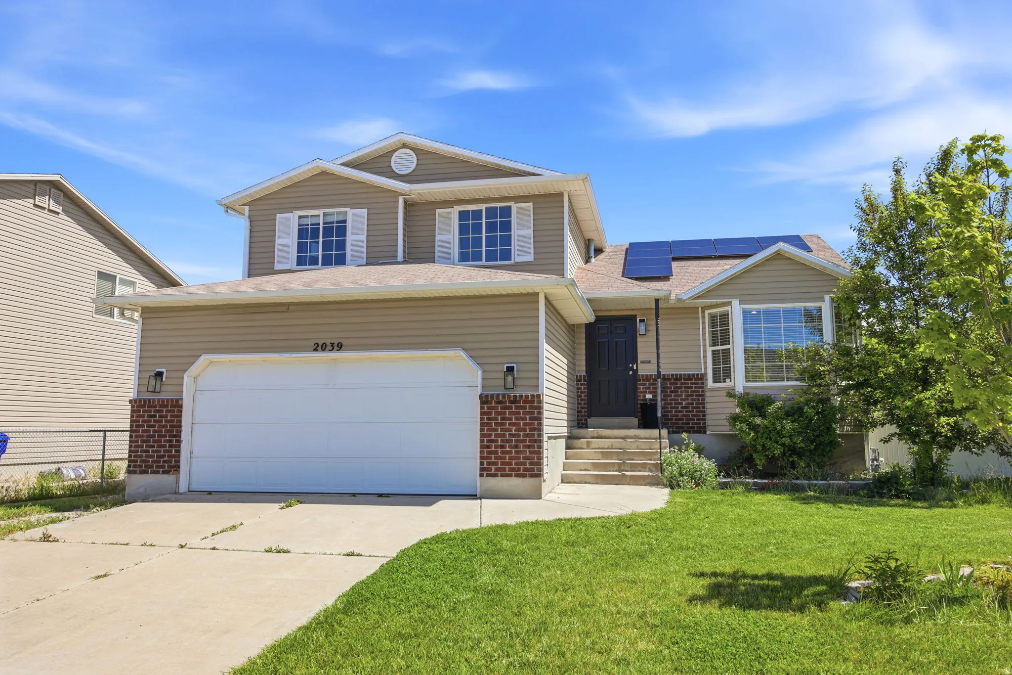 Traditional home with brick siding, roof mounted solar panels, concrete driveway, a front yard, and roof with shingles