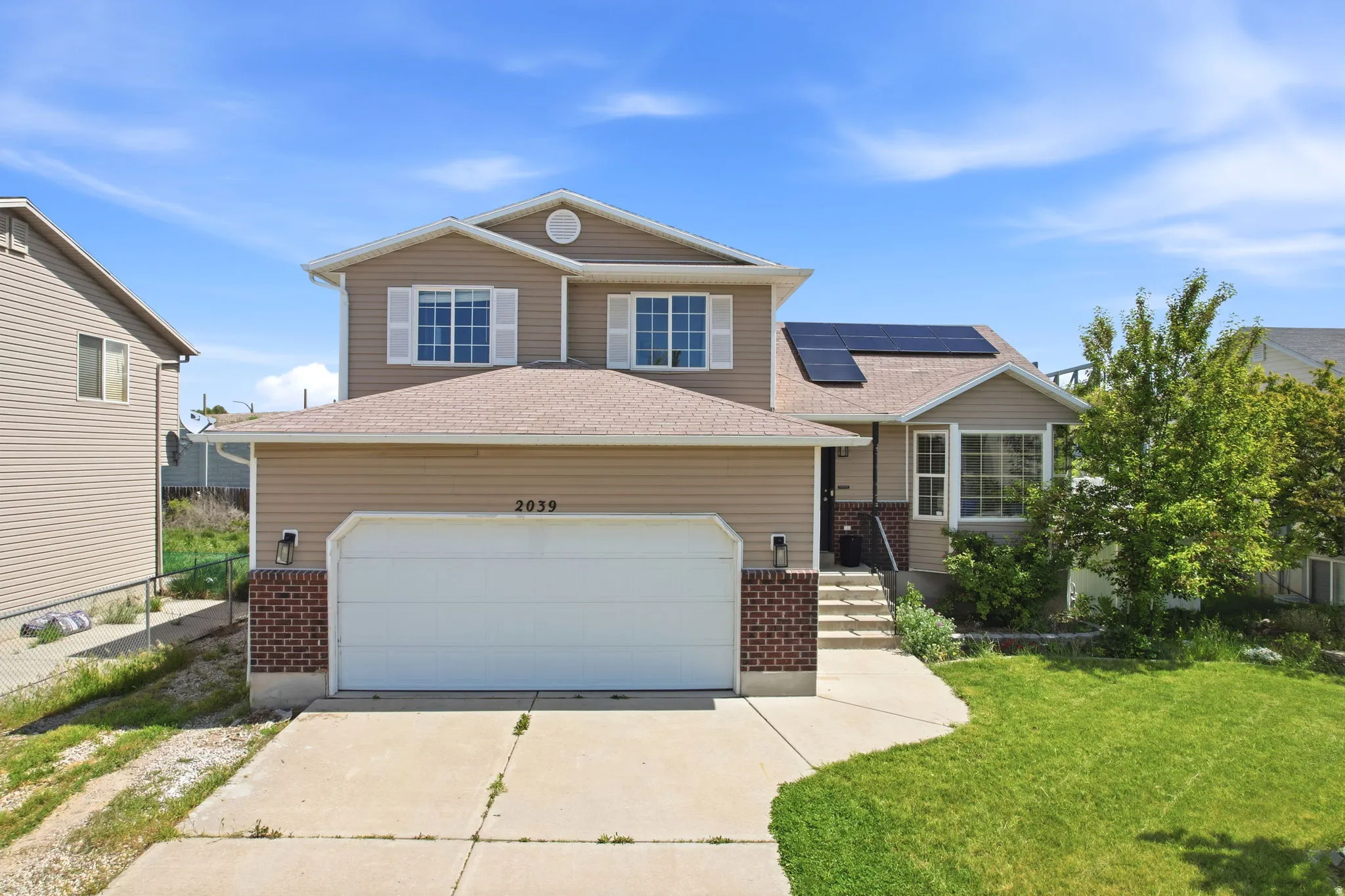 View of front of home featuring brick siding, driveway, solar panels, and a garage