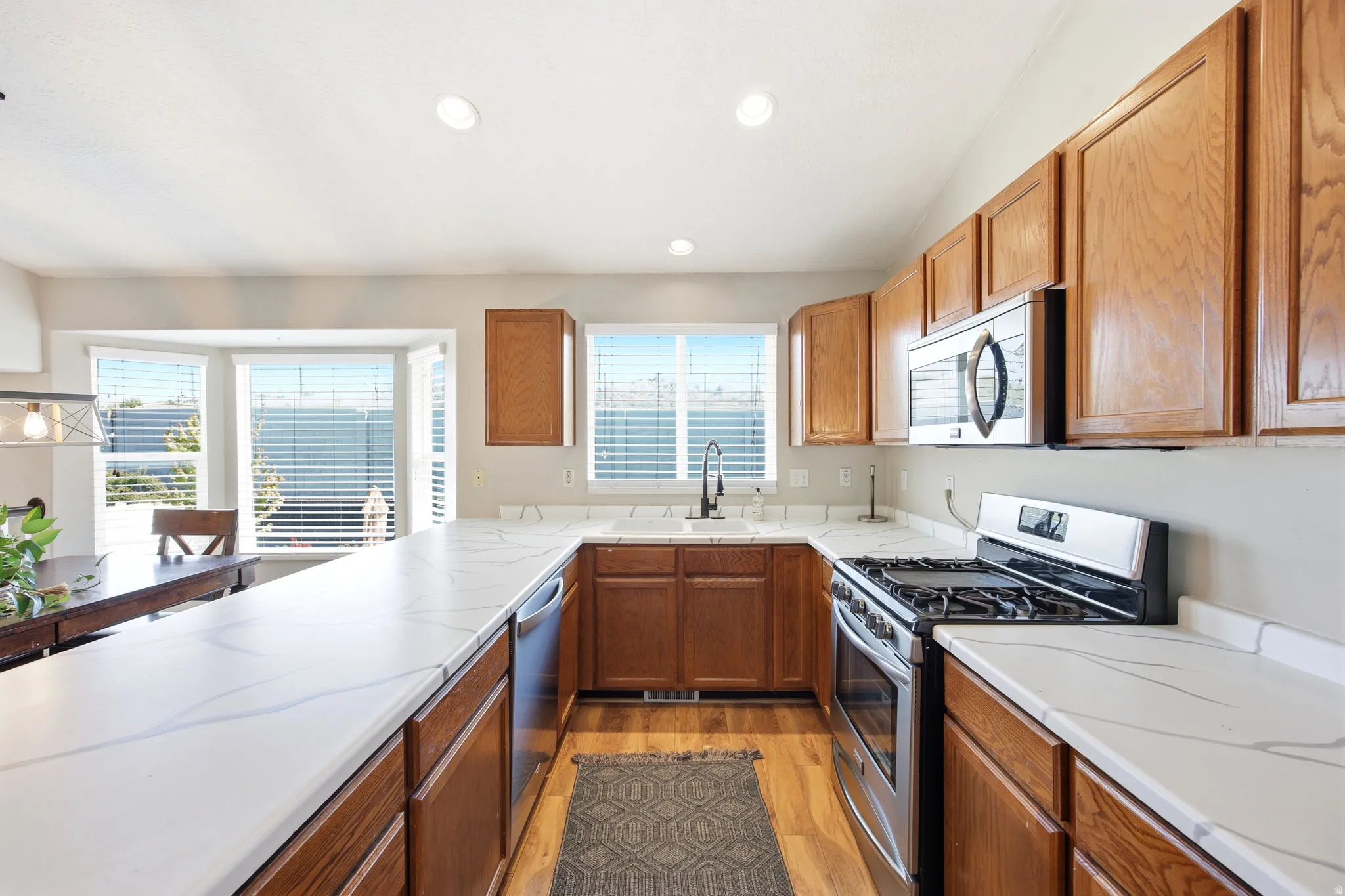 Kitchen featuring stainless steel appliances, wood finish cabinets, light countertops, light wood-style flooring, and recessed lighting