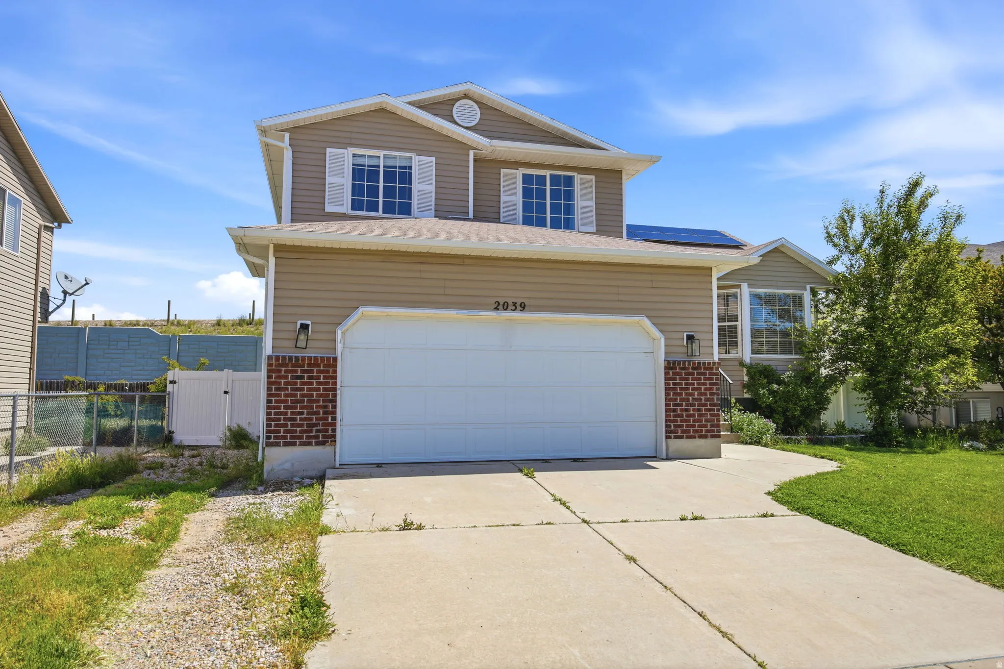 Traditional home featuring brick siding, concrete driveway, roof mounted solar panels, and a gate