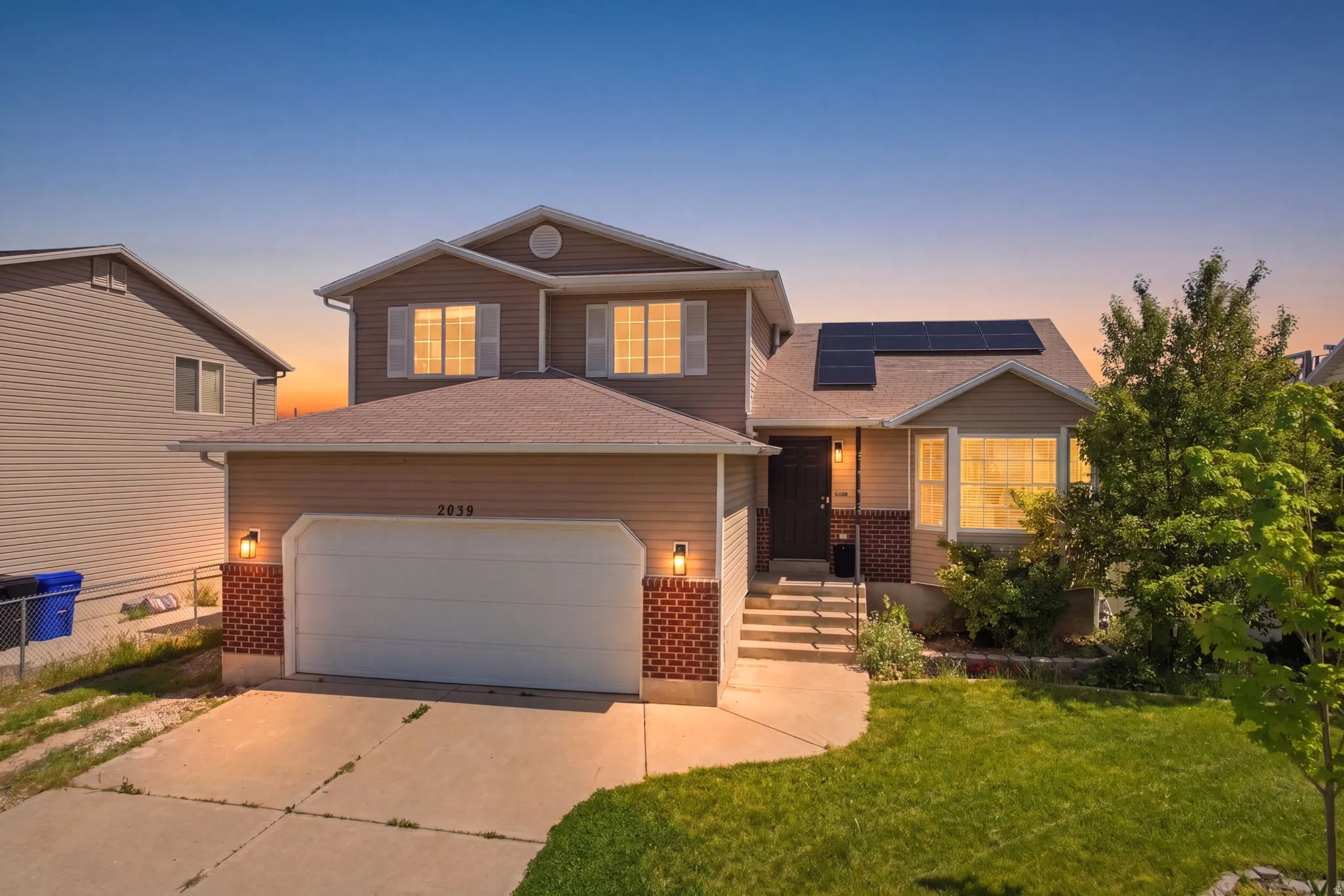 View of front of home with brick siding, roof mounted solar panels, concrete driveway, a front lawn, and roof with shingles