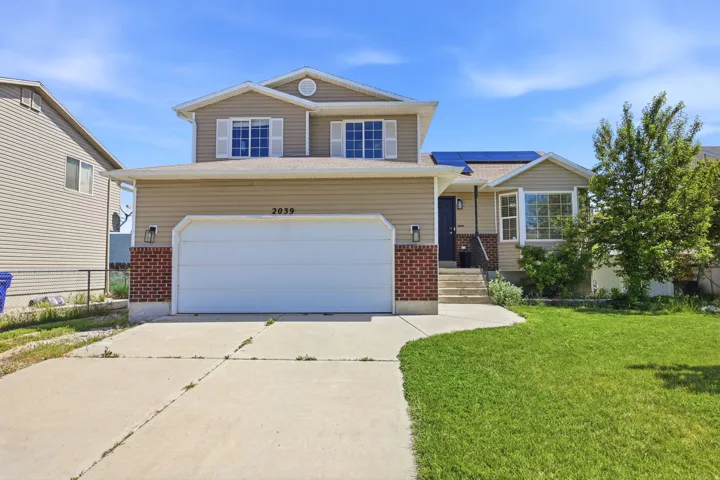 Traditional-style home featuring brick siding, roof mounted solar panels, concrete driveway, an attached garage, and a front lawn