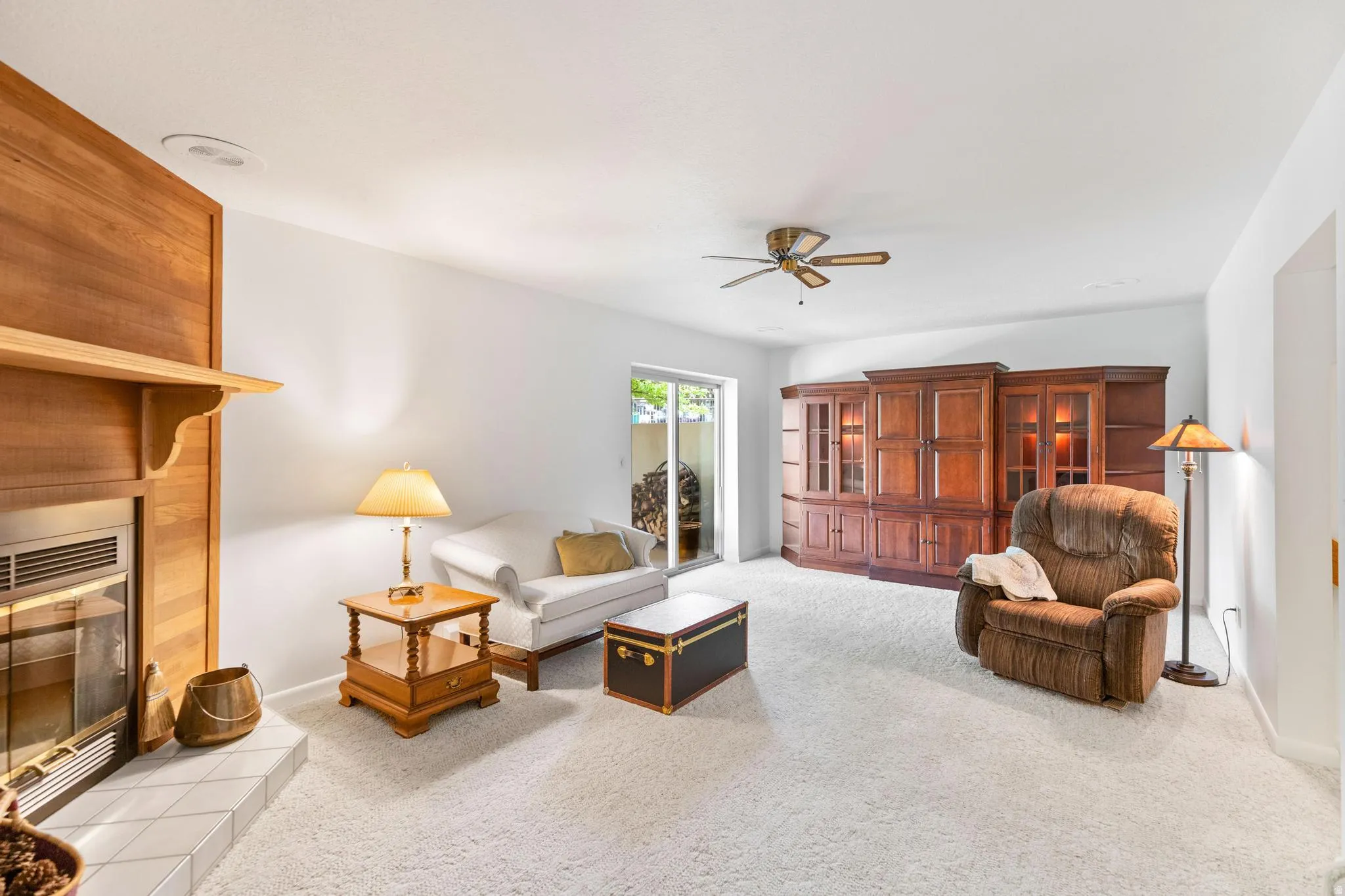 Living area with light carpet, ceiling fan, and a tiled fireplace