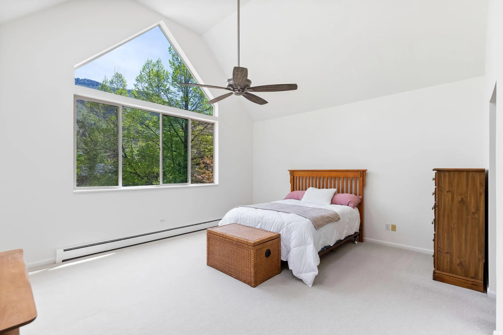 Bedroom featuring a baseboard heating unit, light colored carpet, multiple windows, a ceiling fan, and a high ceiling
