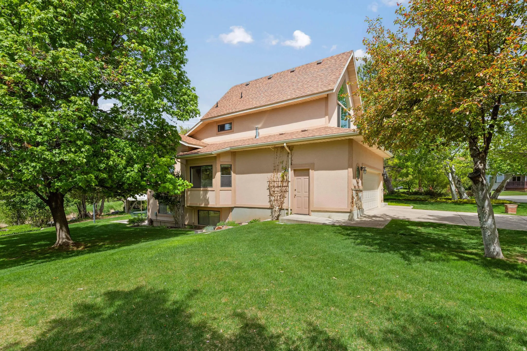 Back of house with a yard, stucco siding, a garage, and driveway