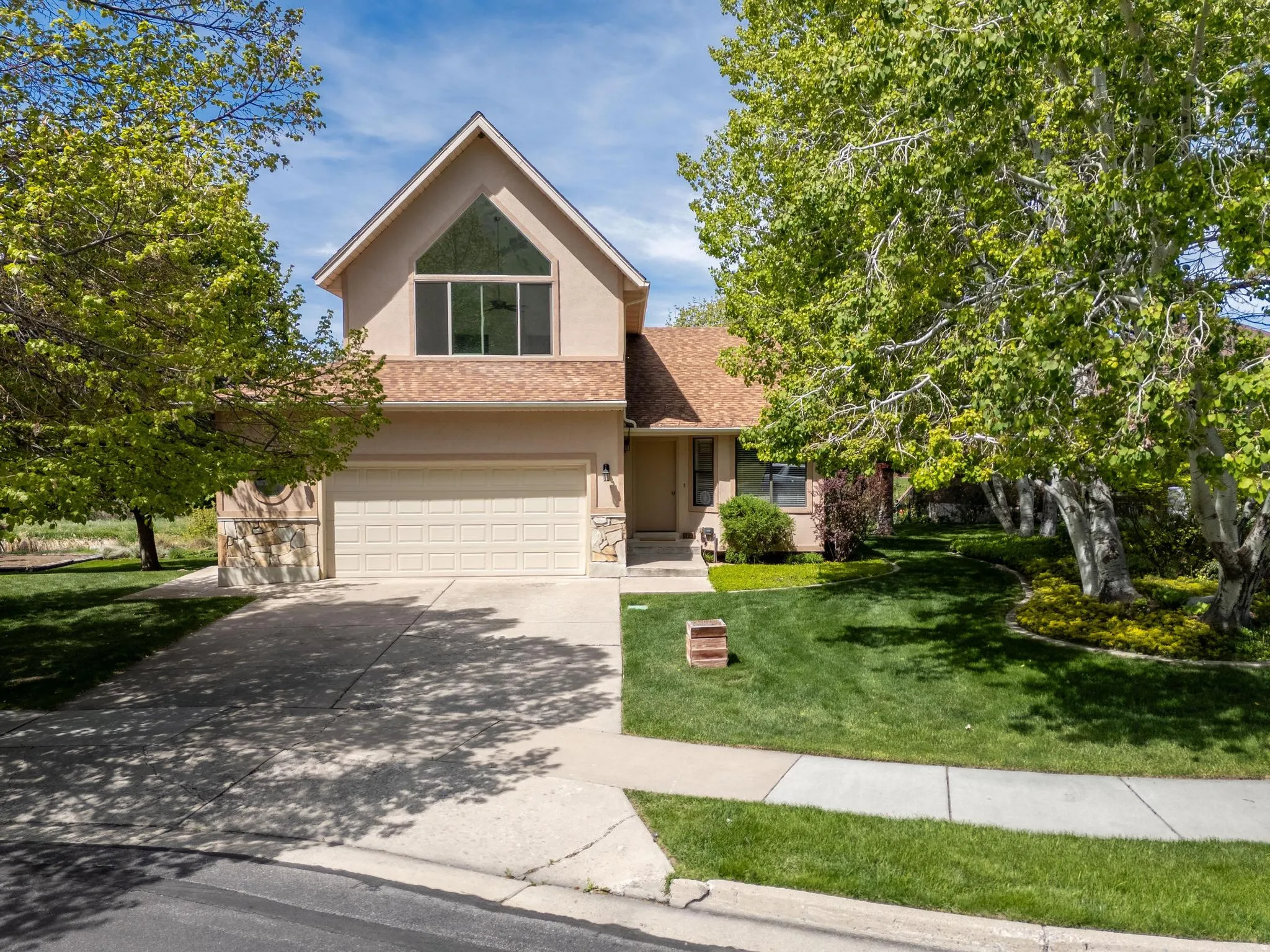 Traditional-style home featuring stone siding, an attached garage, stucco siding, driveway, and a front yard