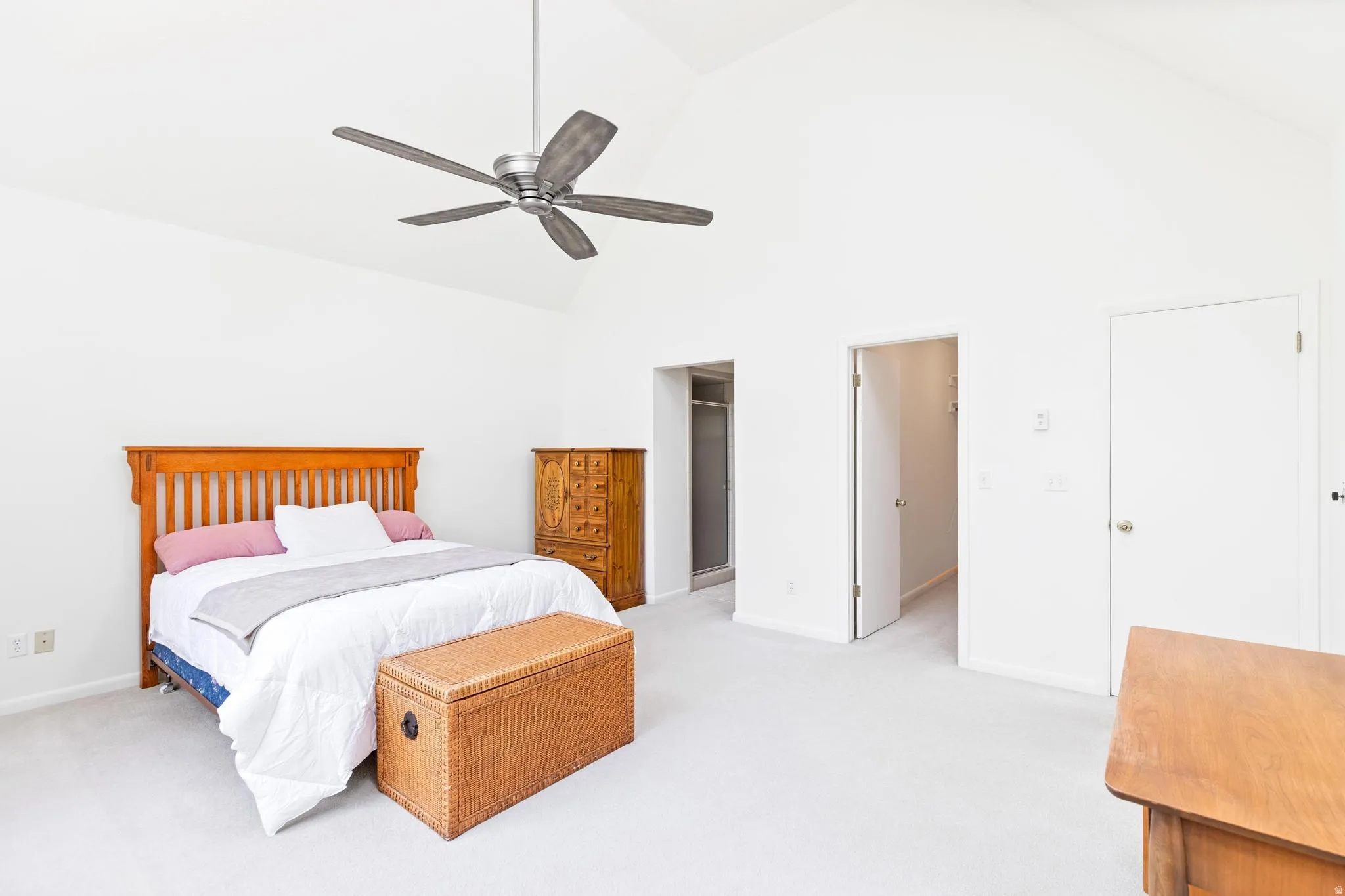 Bedroom featuring a spacious closet, light colored carpet, vaulted ceiling, and a ceiling fan