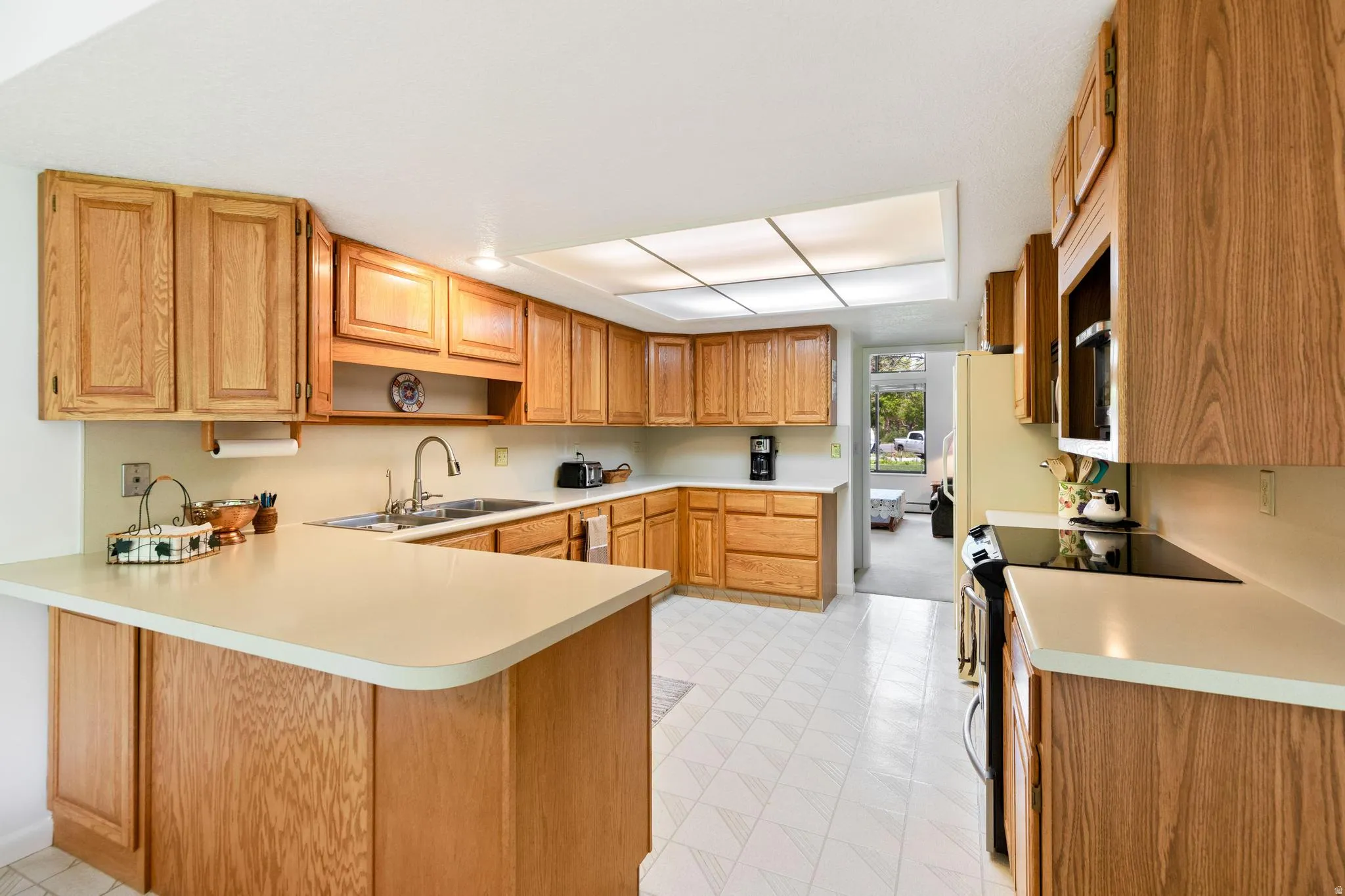 Kitchen with electric stove, a peninsula, wood finish cabinets, and light countertops