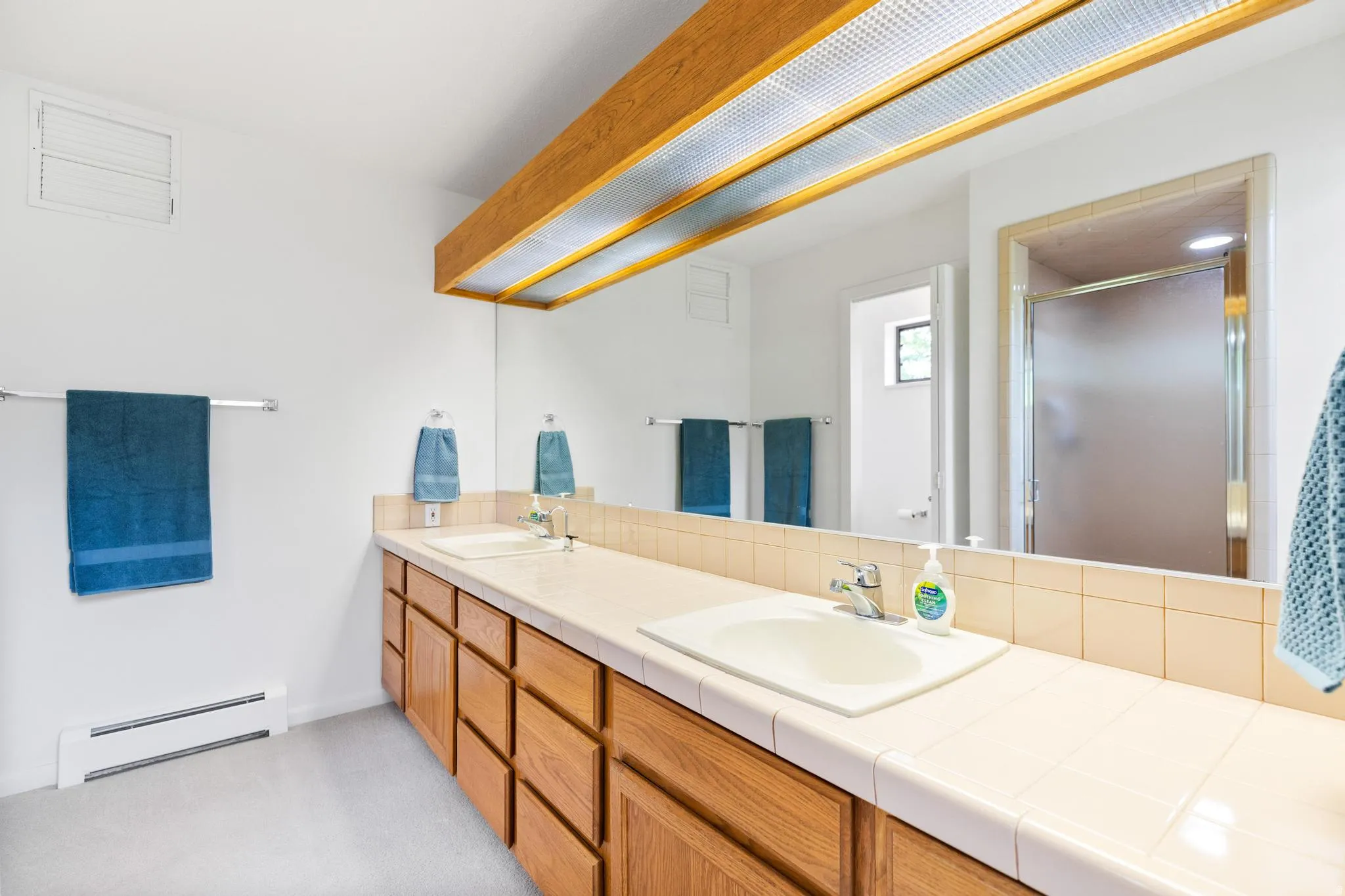 Bathroom featuring double vanity, a baseboard heating unit, and a stall shower