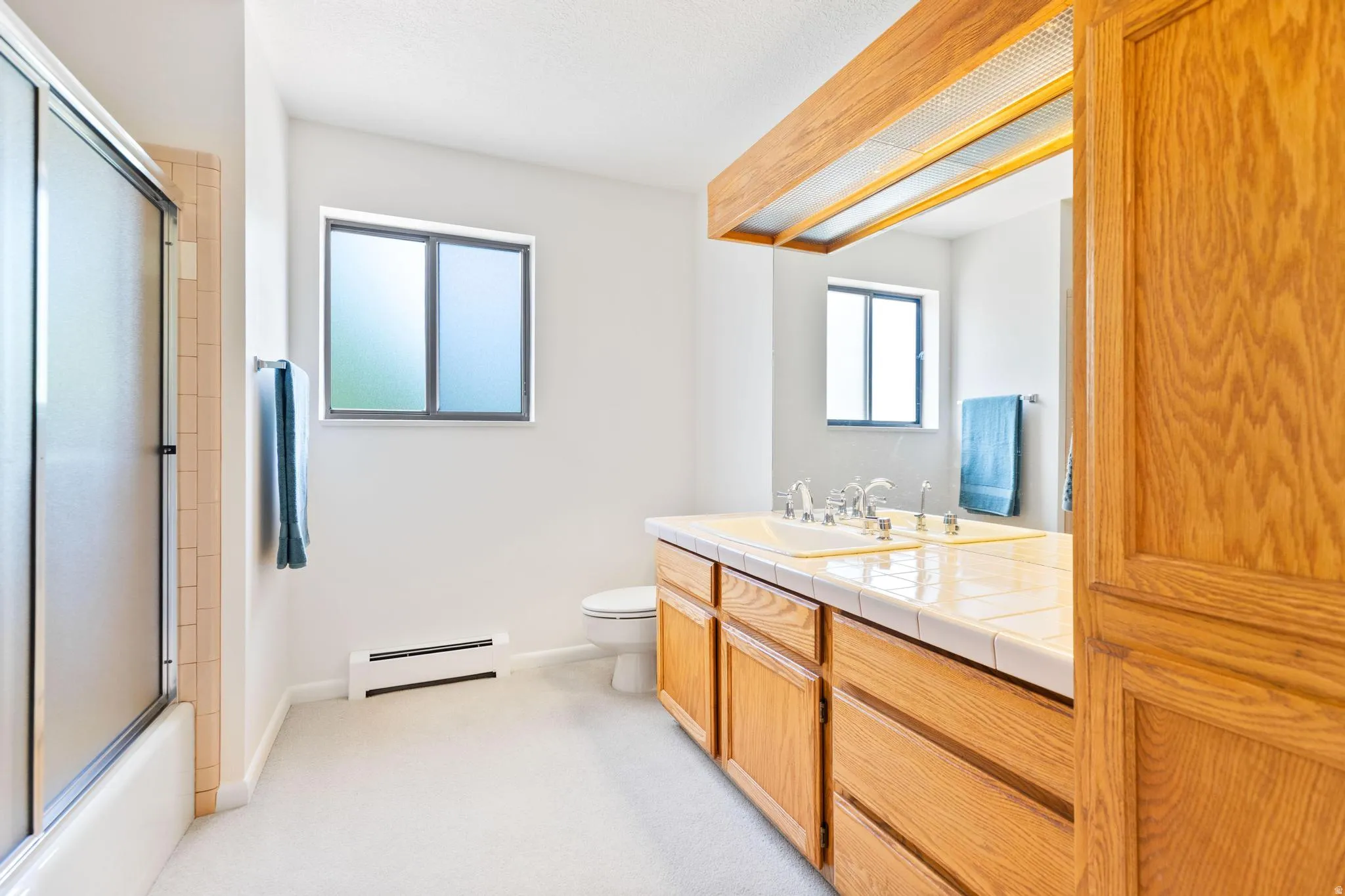 Full bathroom with vanity, a baseboard radiator, light carpet, and bath / shower combo with glass door