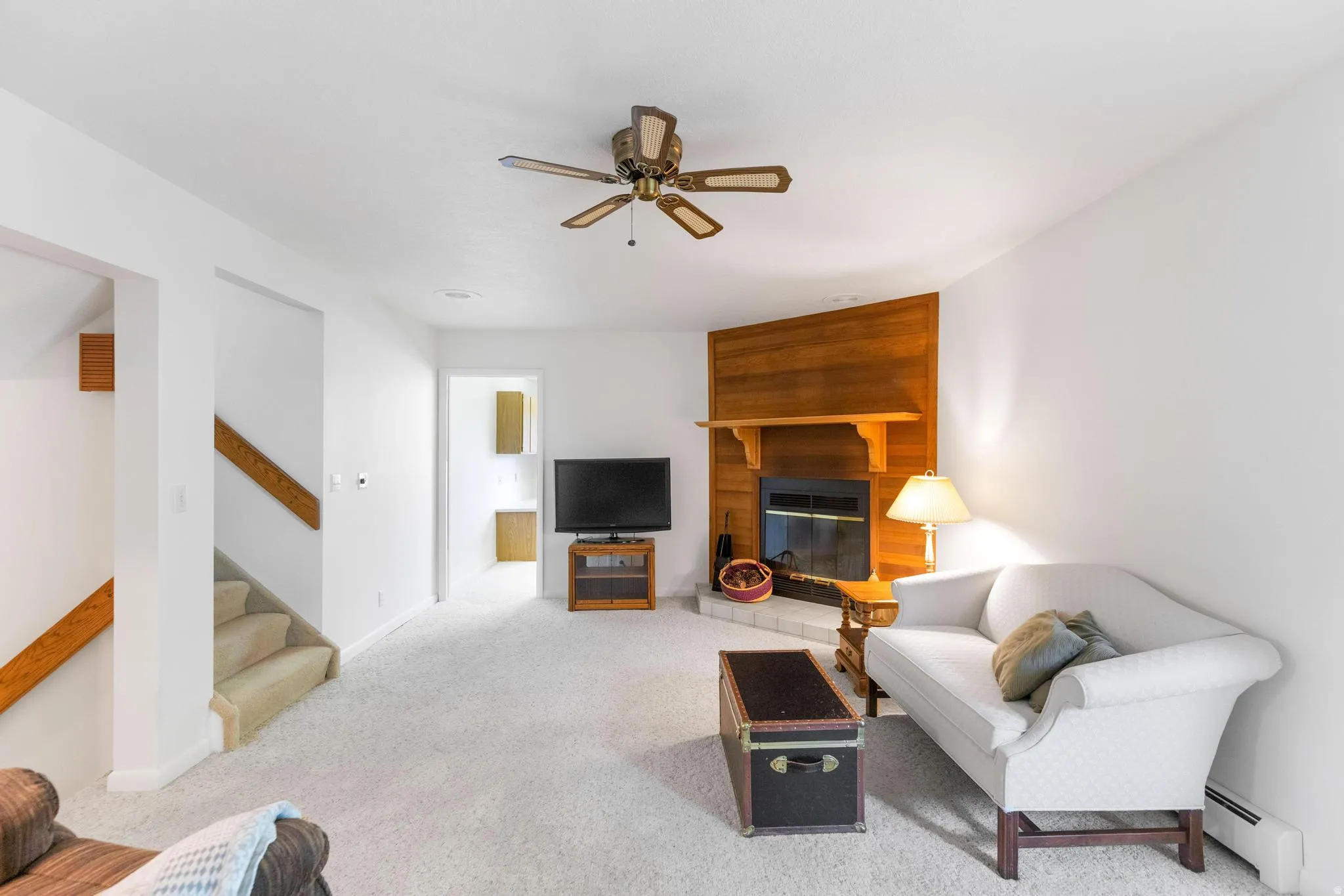 Living room featuring light colored carpet, a ceiling fan, a baseboard radiator, and a fireplace