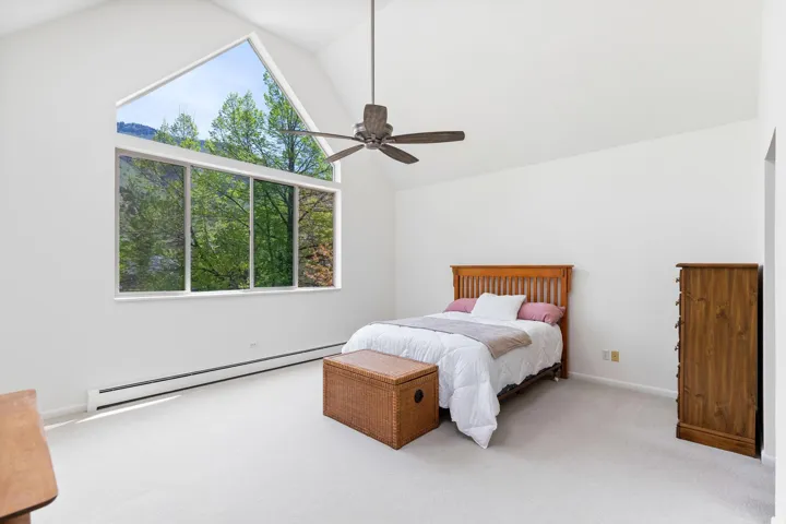 Bedroom featuring a baseboard heating unit, light colored carpet, multiple windows, a ceiling fan, and a high ceiling