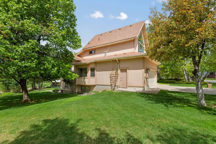 Back of house with a yard, stucco siding, a garage, and driveway
