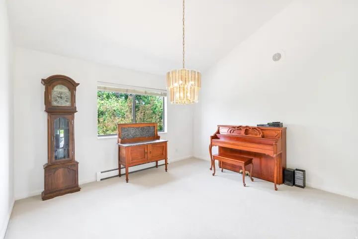 Living area with light colored carpet, lofted ceiling, a baseboard heating unit, and a chandelier