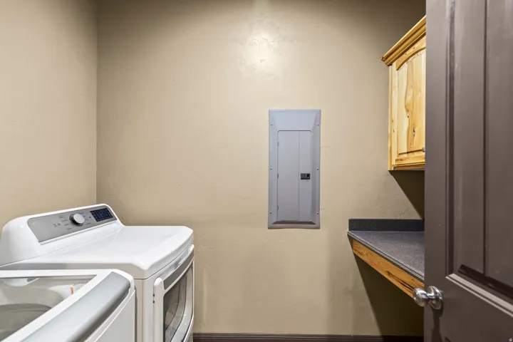 Laundry room featuring a textured wall, electric panel, washer and dryer, and cabinet space
