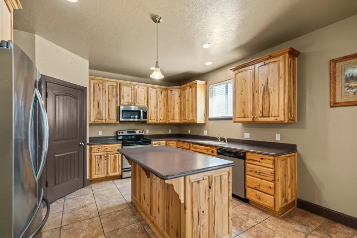Kitchen featuring stainless steel appliances, dark countertops, pendant lighting, a kitchen island, and a textured ceiling