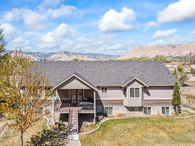 Rear view of property with a mountain view, stucco siding, a lawn, brick siding, and a shingled roof