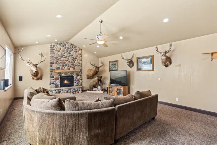 Carpeted living area featuring ceiling fan and a stone fireplace