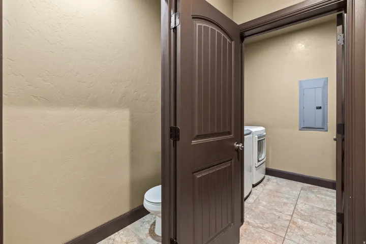 Bathroom with electric panel, a textured wall, washing machine and clothes dryer, and light tile patterned floors