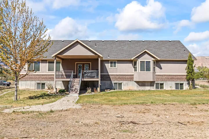 View of front facade featuring a front yard, a shingled roof, a balcony, stucco siding, and brick siding