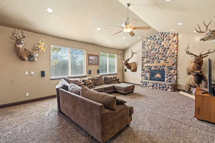 Living room with a stone fireplace, carpet, a ceiling fan, and a textured ceiling