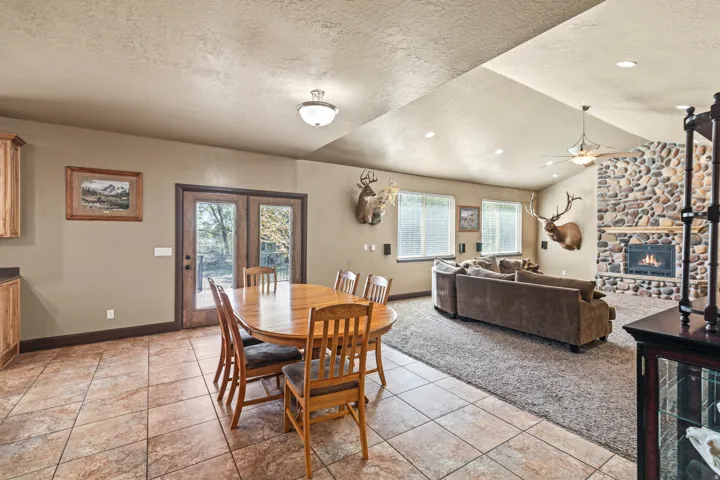 Dining room featuring a textured ceiling, a fireplace, a ceiling fan, light tile patterned flooring, and french doors