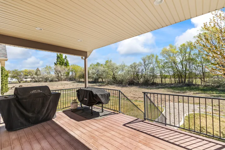 Wooden terrace with a grill, a lawn, and view of scattered trees