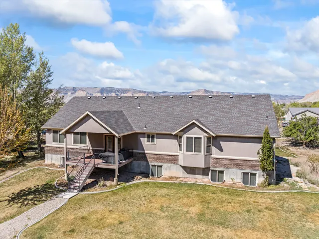 Back of property featuring a lawn, a shingled roof, a mountain view, brick siding, and stucco siding