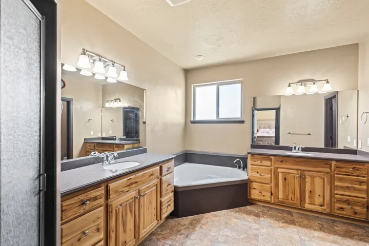 Bathroom with two vanities, a bath, a textured ceiling, and light stone finish floors