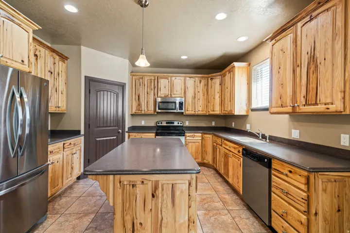 Kitchen with stainless steel appliances, a center island, dark countertops, decorative light fixtures, and light tile patterned floors